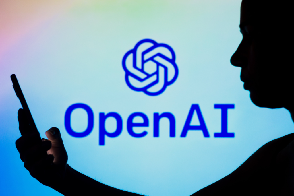 Person silhouetted holding phone in front of OpenAI logo